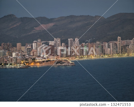 vibrant shoreline with city lights, dusk at beach showcasing illuminated promenade and mountain 132471553