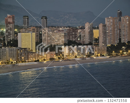luminous coast and cityscape, quiet night by shore with illuminated hotels and distant mountains luminous coast and cityscape, quiet night by shore with illuminated hotels and distant mountains 132471558