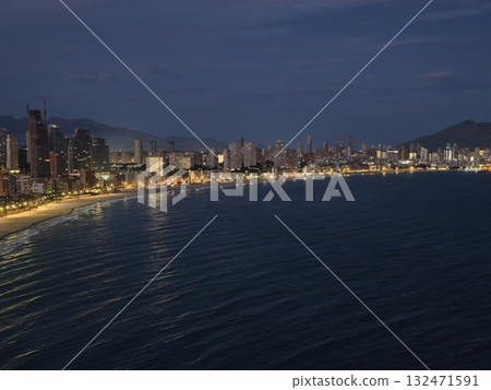 peaceful nighttime coastal panorama showcasing lit promenade and distant skyscraper silhouette 132471591