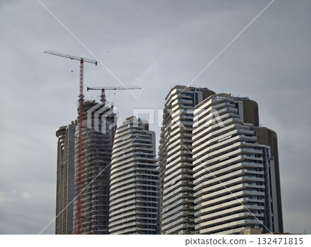 construction with cranes and scaffolding, cityscape featuring exposed frameworks and overcast skies 132471815