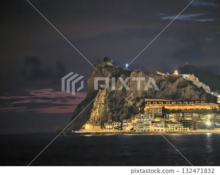 lighthouse overlooking peaceful rocky coast, scenic nighttime setting with glowing lights 132471832