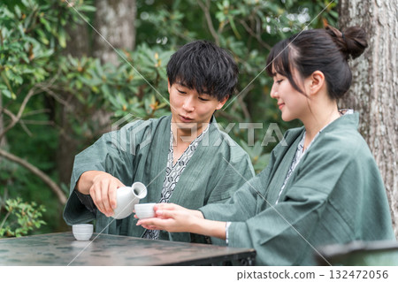 一對穿著浴衣的夫婦在傳統日式旅館的花園露臺上喝清酒 132472056