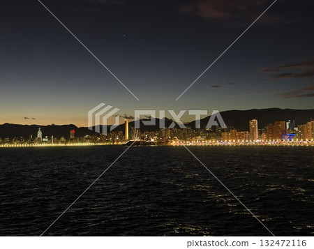 seaside evening reflections, calm coastal panorama during sunset with vibrant promenade illumination seaside evening reflections, calm coastal panorama during sunset with vibrant promenade illumination 132472116