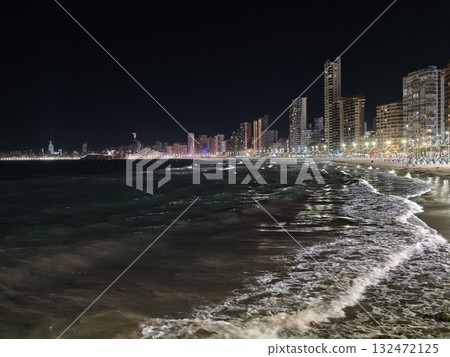 serene nighttime ocean, nighttime shoreline with shimmering water and illuminated cityscape horizon 132472125