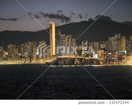 seaside night skyline, lively boulevard stretches below shimmering water with luminous tower seaside night skyline, lively boulevard stretches below shimmering water with luminous tower 132472144