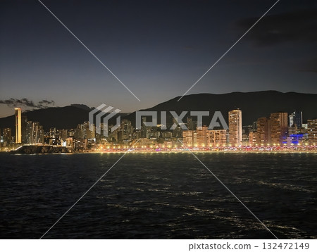 tranquil seaside panorama during twilight featuring illuminated waterfront and distant mountains 132472149