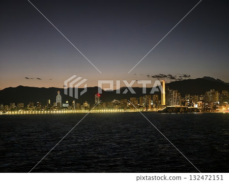 bright urban horizon view, serene city skyline illuminated by landmark tower and coastal reflections 132472151