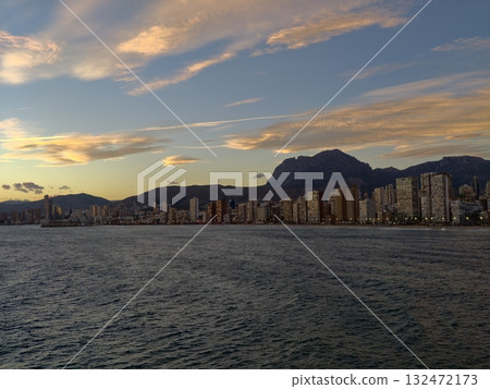 evening seaside panorama, sunset casting warm light on peaceful coastal cityscape with mountains 132472173
