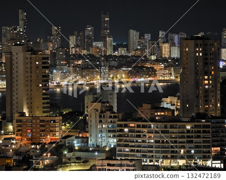 bright cityscape by water, nighttime city silhouette reflecting on calm harbor waters at dusk 132472189