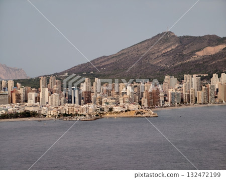 calm waterfront scene with distant hills, tranquil bay view featuring glowing towers and soft clouds 132472199