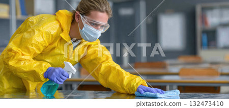 Person wearing protective gear disinfects surface with cleaning spray to prevent virus spread showing care for mysophobia and hygiene safety 132473410