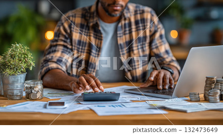 Person calculating company income and expenses on laptop surrounded by financial documents and coins, focused on budgeting and accounting tasks 132473649
