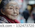 Aging woman with glasses, smiling warmly in busy urban setting, showcasing importance of geriatric care 132473720