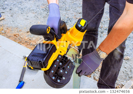 Worker is operating handheld electric saw tool to cutting metal while working in construction site. 132474656