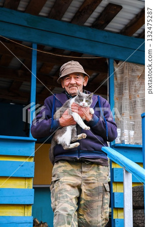 Elderly Russian man standing on the porch of his rural home, holding his gray and white cat with care and warmth, simple village life moment. Elderly Russian man standing on the porch of his rural home, holding his gray and white cat with care and warmth, simple village life moment. 132475287