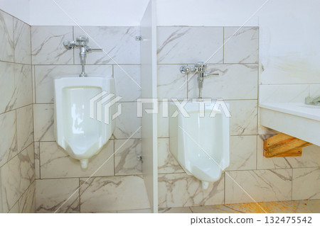 Two sleek white urinals are installed in modern restroom with light marble tile design. 132475542