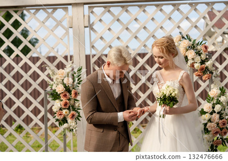 Couple exchanges wedding rings during outdoor ceremony surrounded by flowers 132476666