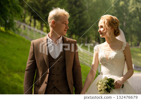 Couple walking hand in hand through a lush park on their wedding day Couple walking hand in hand through a lush park on their wedding day 132476679