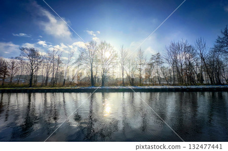 A Serene and Tranquil Winter Reflection at the Riverbank with Beautiful Glowing Sunlight A Serene and Tranquil Winter Reflection at the Riverbank with Beautiful Glowing Sunlight 132477441