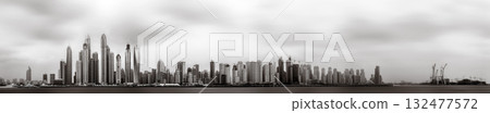 Monochrome city skyline with tall skyscrapers reflecting on calm water under a cloudy sky, Dubai Marina bay UAE 132477572