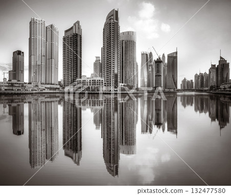 Monochrome city skyline with tall skyscrapers reflecting on calm water under a cloudy sky, Dubai Marina bay UAE Monochrome city skyline with tall skyscrapers reflecting on calm water under a cloudy sky, Dubai Marina bay UAE 132477580