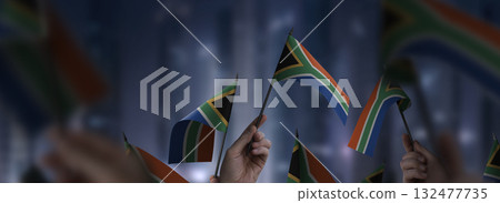 South Africa flags in their hands on a blurred urban background South Africa flags in their hands on a blurred urban background 132477735