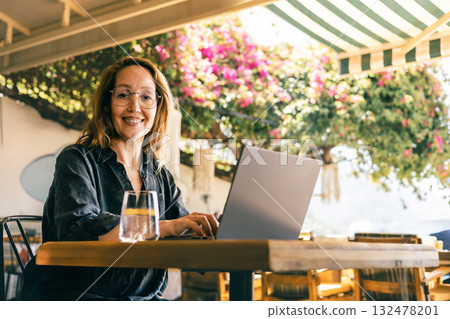 Happy Woman Working on Laptop Outdoors Under Blooming Tree in Sunny Cafe Environment Happy Woman Working on Laptop Outdoors Under Blooming Tree in Sunny Cafe Environment 132478201