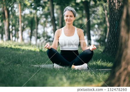 Serene Middle-Aged Woman Practicing Sukhasana Meditation Outdoors in Peaceful Green Park 132478260