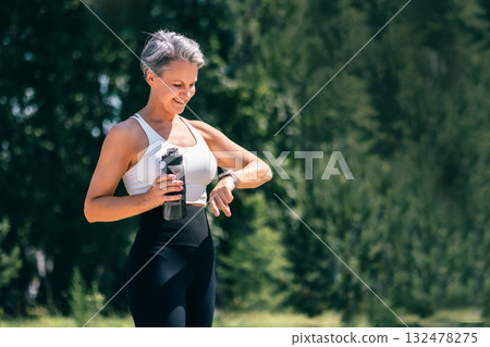 Smiling Mature Woman Checking Smartwatch After Outdoor Workout with Water Bottle Smiling Mature Woman Checking Smartwatch After Outdoor Workout with Water Bottle 132478275