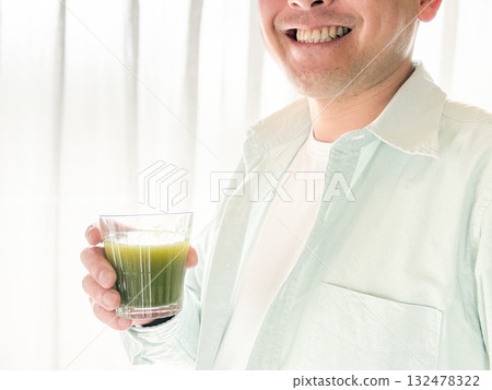 一名三十多歲的男子正在喝綠色果汁 132478322