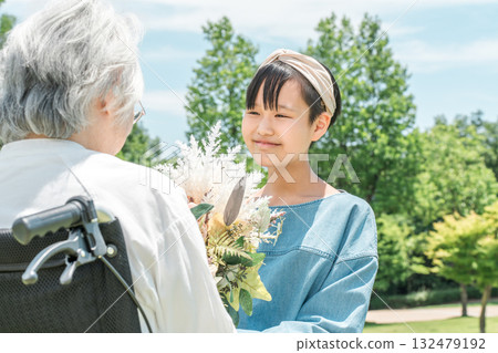 Smiling granddaughter presents a bouquet of flowers to her grandmother in a wheelchair Smiling granddaughter presents a bouquet of flowers to her grandmother in a wheelchair 132479192