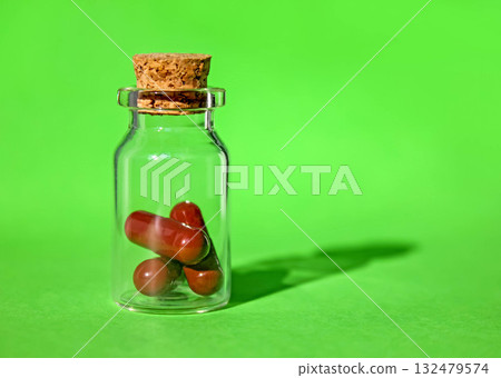 Glass bottle with cork and brown pills on green background with place for text. Glass bottle with cork and brown pills on green background with place for text. 132479574