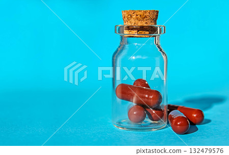 Closeup medicine in glass bottle with wooden cork on blue background. Closeup medicine in glass bottle with wooden cork on blue background. 132479576
