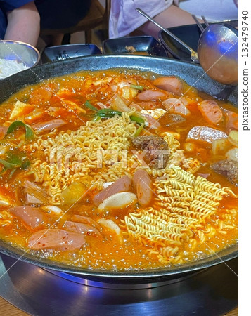A hearty bowl of Budaejjigae (Korean Army Stew), filled with sausage, tofu, kimchi, and noodles in a spicy broth. This flavorful dish brings warmth and comfort, perfect for sharing. 132479740