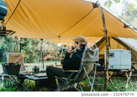 Male camper drinking coffee under a tarp at a campsite in autumn and winter 132479774