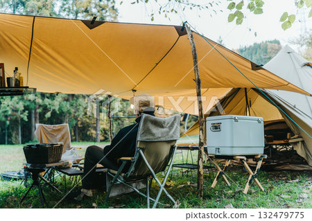 Male camper drinking coffee under a tarp at a campsite in autumn and winter 132479775
