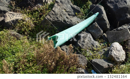 A broken kayak rests among the rocks on the seashore. A broken kayak rests among the rocks on the seashore. 132481164