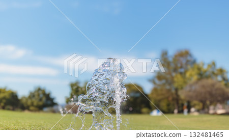 Dripping drops of sparkling water against the background of blue sky and park Dripping drops of sparkling water against the background of blue sky and park 132481465