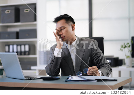 Sad businessman is sitting at table, covering his face with his hand. On desk is laptop, tablet computer, Stress. 132482994
