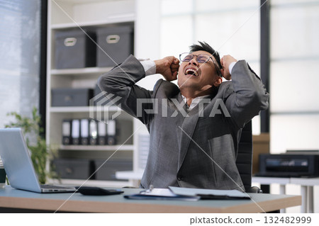 Sad businessman is sitting at table, covering his face with his hand. On desk is laptop, tablet computer, Stress. 132482999