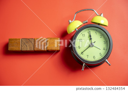 Green alarm clock with row of wooden cubes on colored background. Empty area for copy space. Concept of time, reminder, or deadline 132484354
