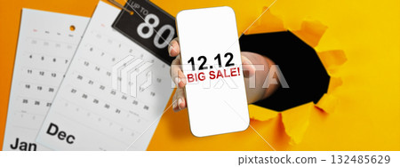 Human hand through hole paper showing 12.12 big sale text on cellphone screen with up to 80% text on the label tag. Copy space. Flash sale concept Human hand through hole paper showing 12.12 big sale text on cellphone screen with up to 80% text on the label tag. Copy space. Flash sale concept 132485629