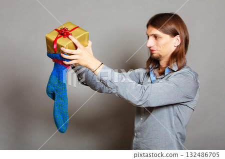 Guy putting wrapped gift in knitted christmas sock Guy putting wrapped gift in knitted christmas sock 132486705