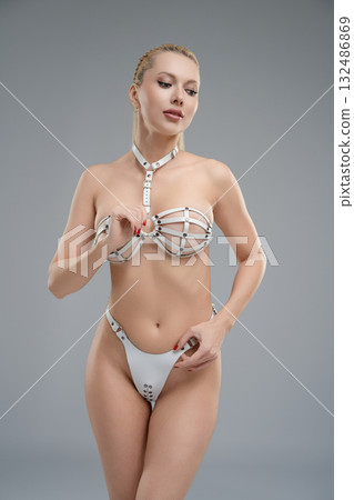 Woman in leather belts poses confidently in a studio setting with a simple gray backdrop 132486869