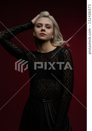Fashionable model strikes a pose against a deep red background during a studio shoot 132486873