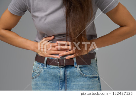 Midsection view of woman pressing lower abdomen with both hands, studio shot Midsection view of woman pressing lower abdomen with both hands, studio shot 132487125