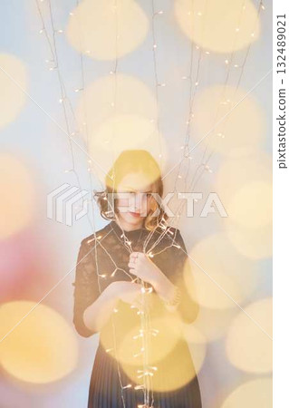 a teenage girl in a dress surrounded by golden Christmas lights a teenage girl in a dress surrounded by golden Christmas lights 132489021