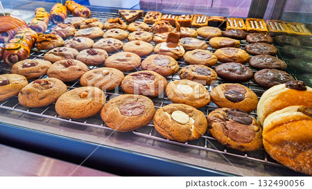 A variety of cookies displayed in a bakery. The assortment includes chocolate chip, oatmeal, and peanut butter cookies on a cooling rack. A variety of cookies displayed in a bakery. The assortment includes chocolate chip, oatmeal, and peanut butter cookies on a cooling rack. 132490056