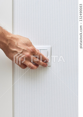 male finger is turning on or off on white light switch on blue wall. 132490083