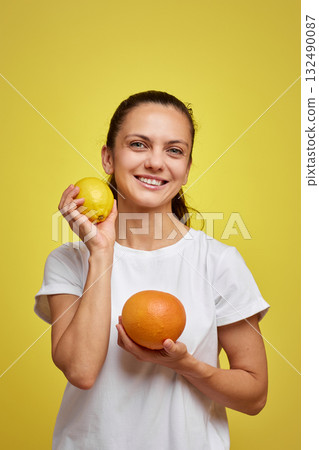happy woman holding fresh lemon and grapefruit on yellow studio background 132490087